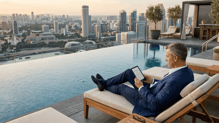 A man sitting beside an infinity pool on a hotel rooftop reading with an eReader.
